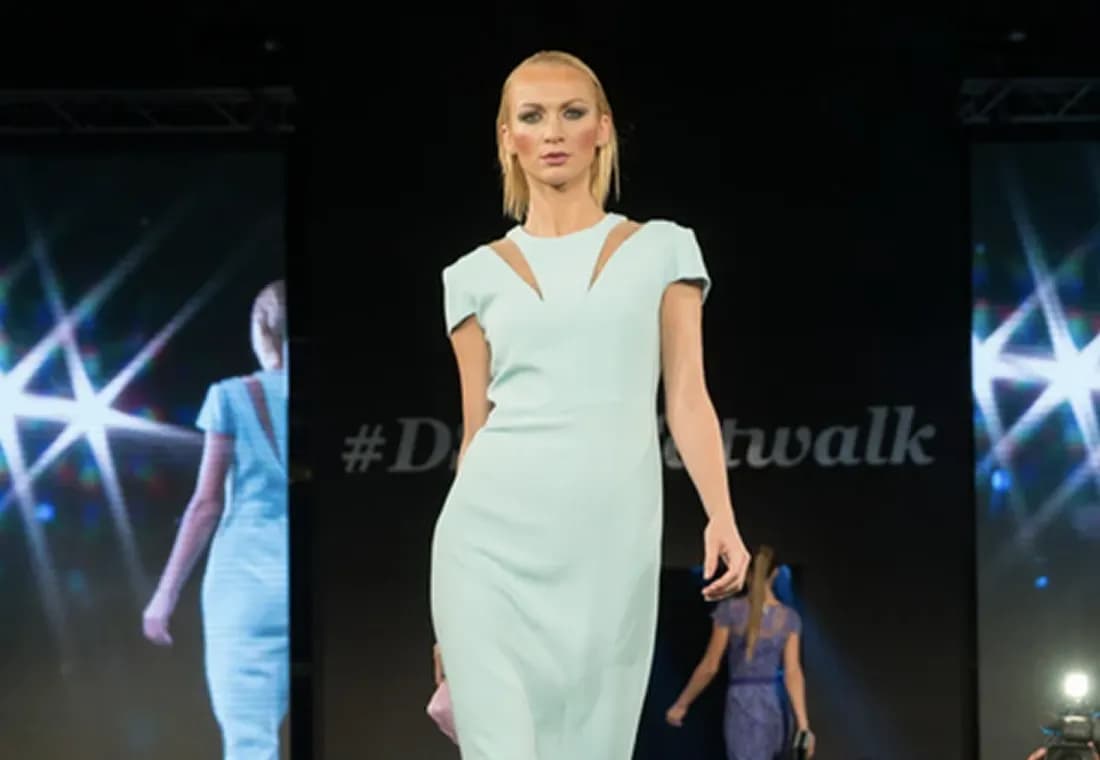 A model presents a designer's dress on a runway between two video screens