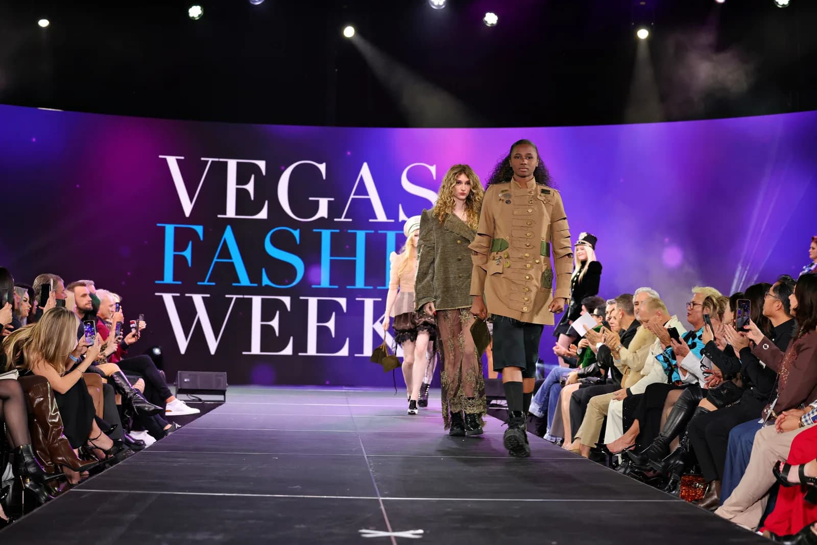 Models on the runway at Vegas Fashion Week®, the event's name on the stage screen behind