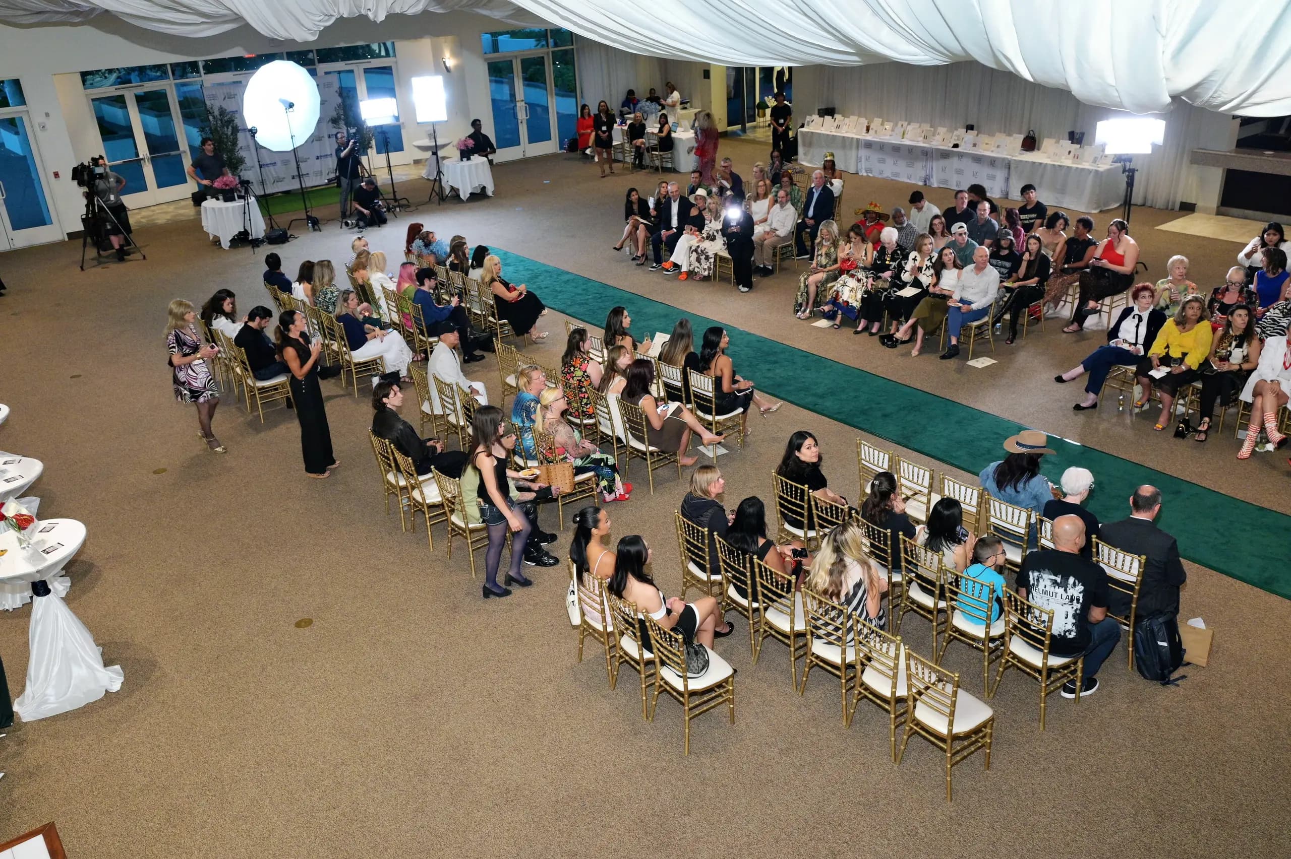 The room at Eco Couture Vegas 2026 from above, with camera crews and lights set up beside the runway